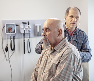 Healthcare provider listening to man's chest with stethoscope.