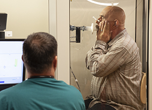 Lab technician performing pulmonary function tests on patient in testing booth.